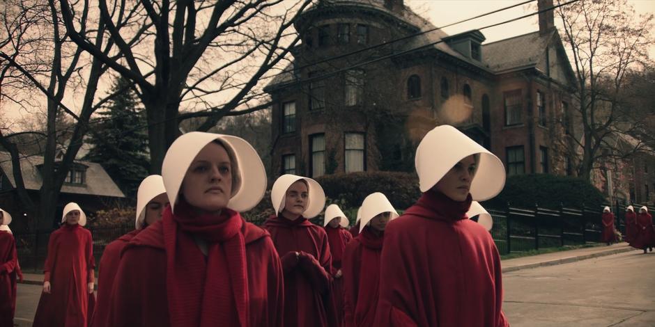 Offred walks across the street with a group of handmaids.