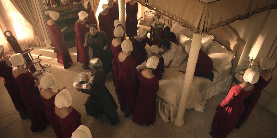 The handmaids surround Janine who is in labor on the bed while Aunt Lydia guides the birthing.