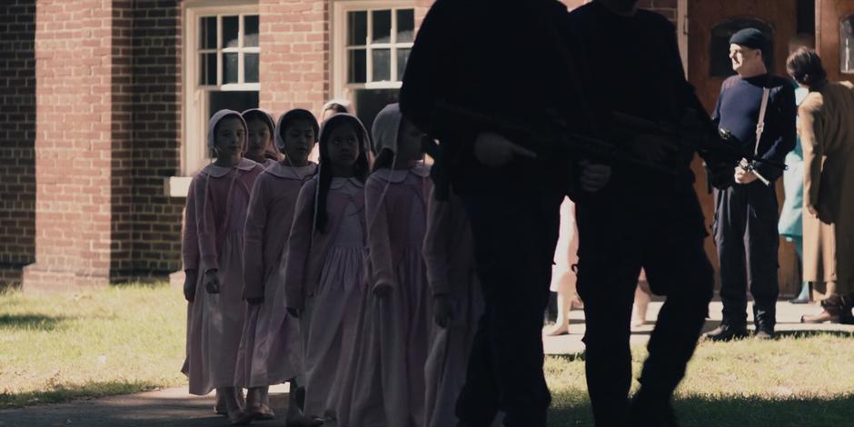 A pair of guards lead a group of girls out of the school.