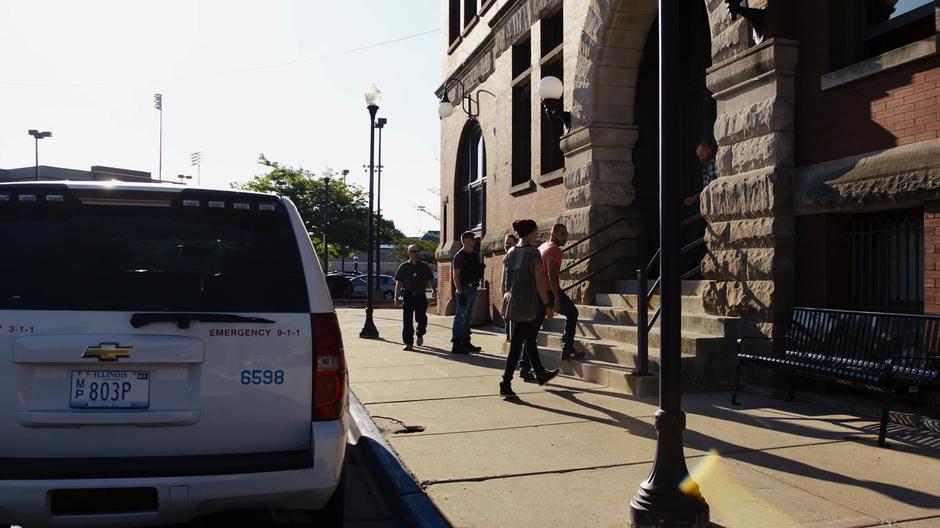 Riley follows Diego up the front steps into the police station.