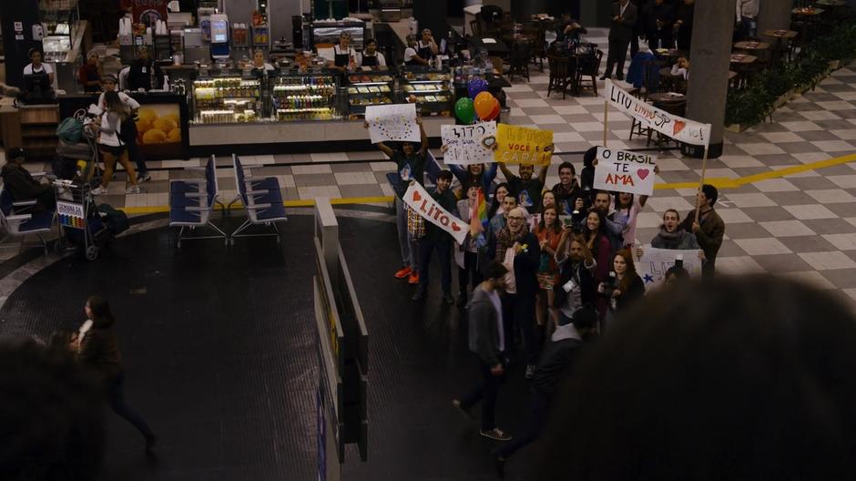 A group of fans and the parade host wait for Lito at the bottom of the escalator.