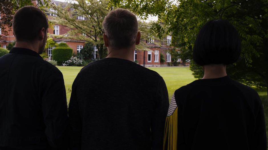 Will, Wolfgang, and Sun look across the lawn towards the manor house.