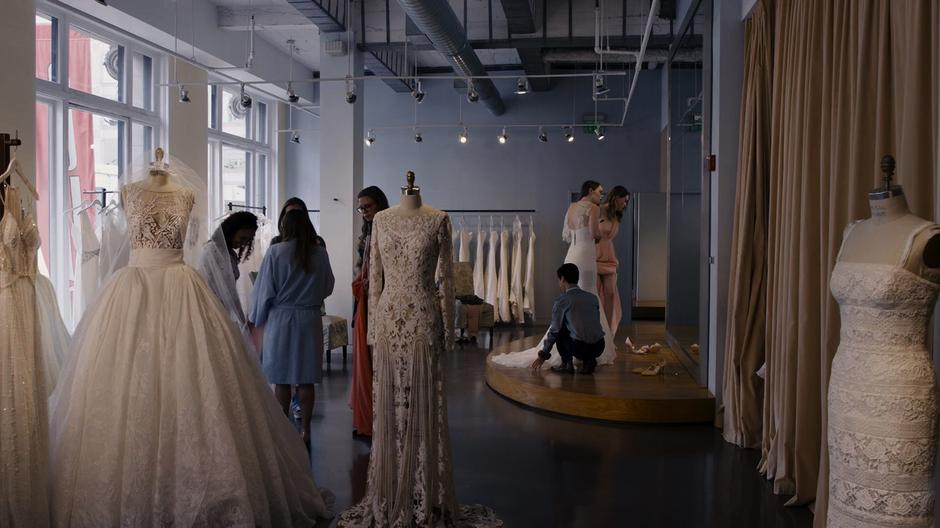 A worker adjusts the trail of Teagan's dress while she and Nomi look at themselves in the mirror.