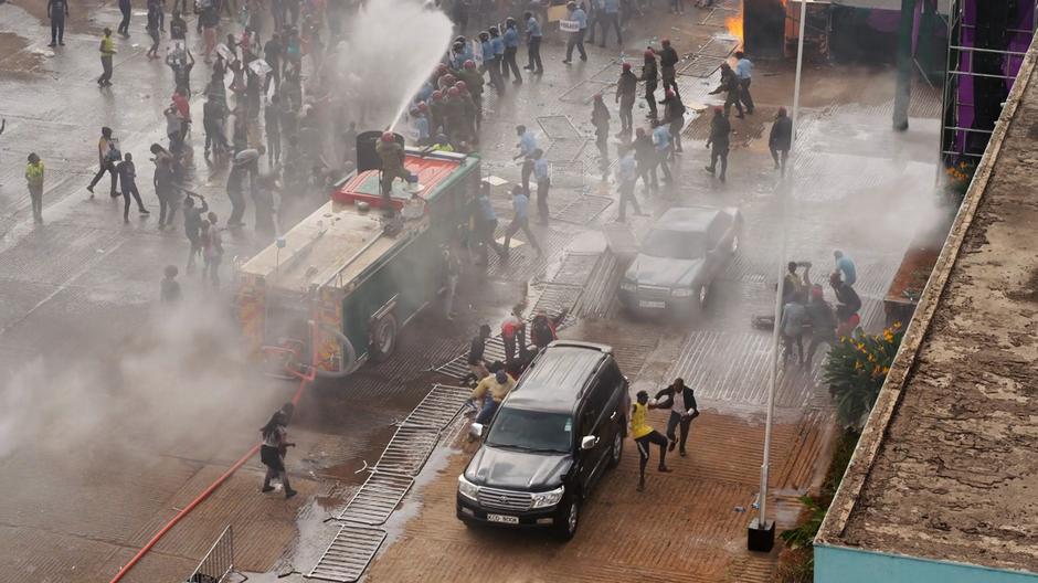 The car with Capheus and Superpower drives away from the rally while the police attempt to quell the riot.