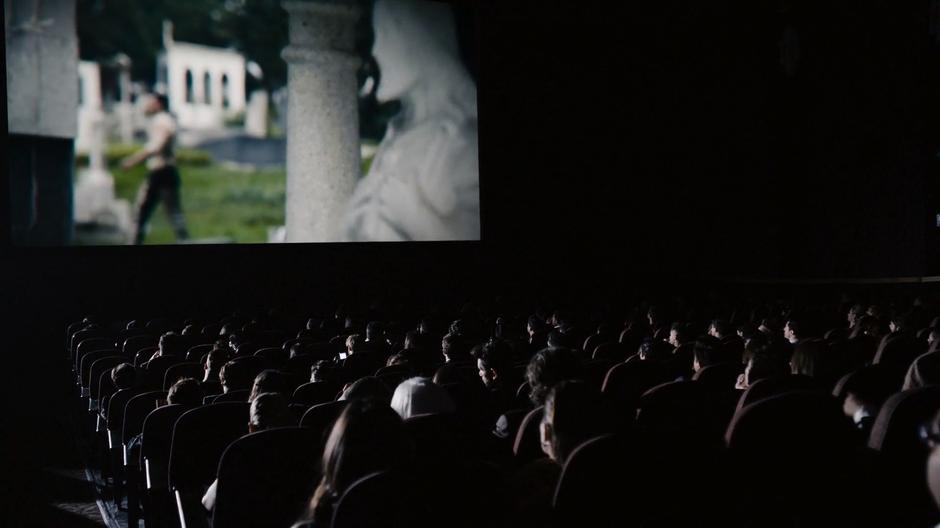 People sit in the theatre watching the movie while Lito's character strolls through the cemetery on screen.