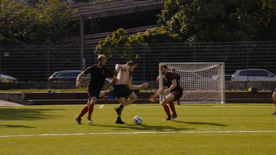 Wolfgang kicks the ball down the field between two opposing players.