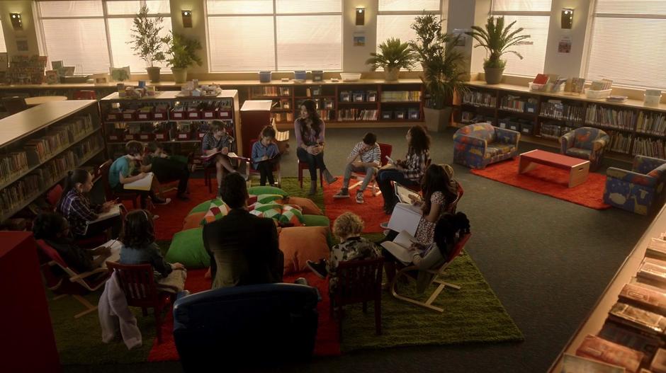 Trixie, Lucifer, and a bunch of students sit around in a circle in the library listening to Madison's teaching.