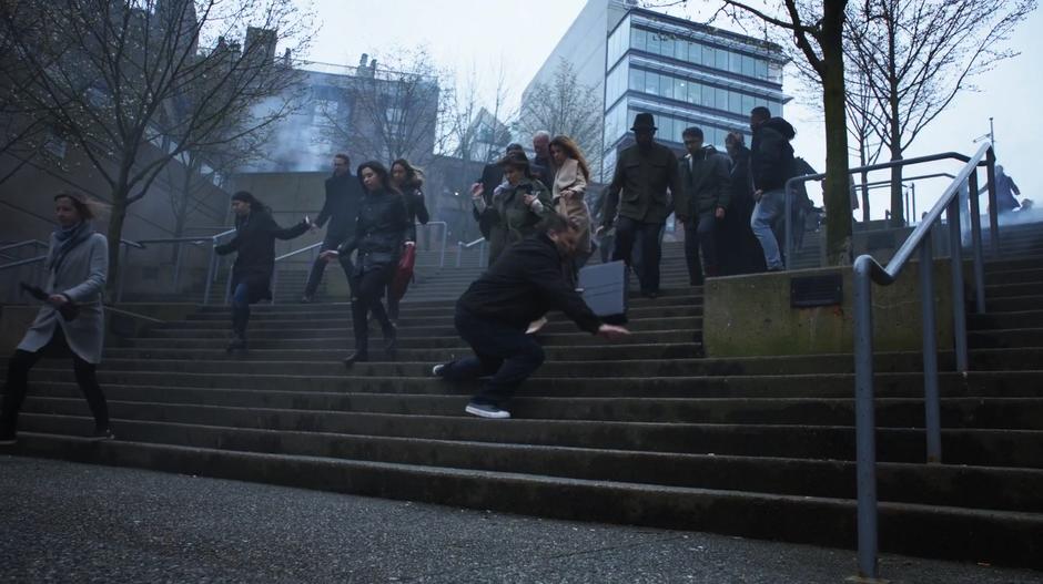 A bunch of people run down the stairs to escape the invaders and one man falls down.