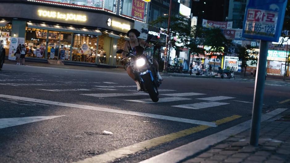 Sun turns the corner on her motorcycle and crosses a crosswalk.