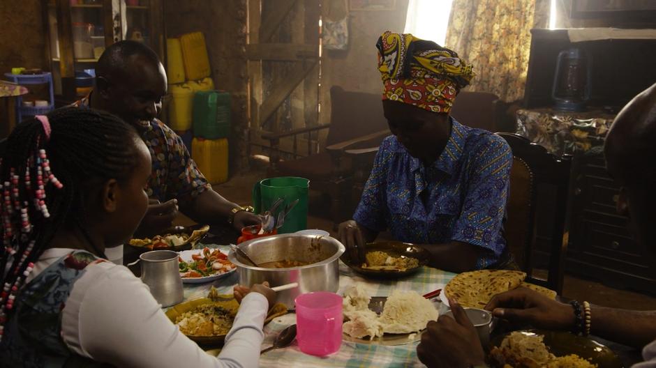 Silas smiles while sharing a meal with Amondi, Shiro, and Capheus.