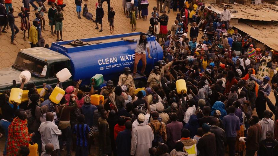 The man in charge of the water truck yells at the crowd while they yell back at him.