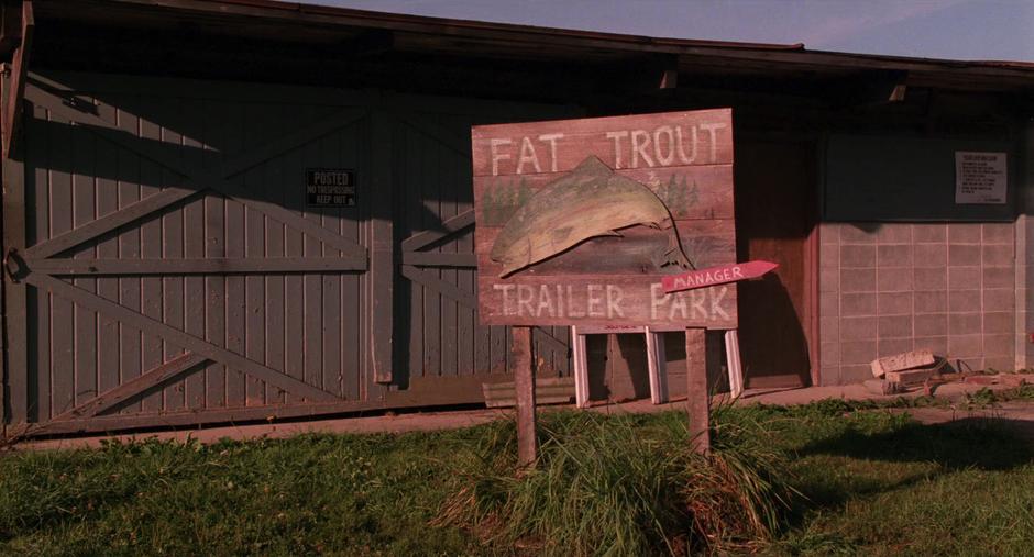 Establishing shot of the Fat Trout Trailer Park sign with a small arrow pointing towards the manager's trailer.