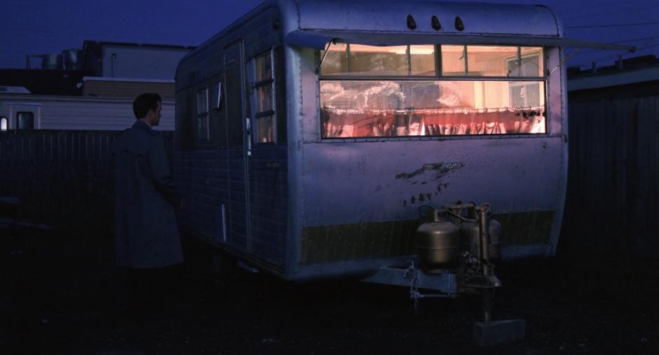 Chet approaches a mysterious lit-up trailer at night.