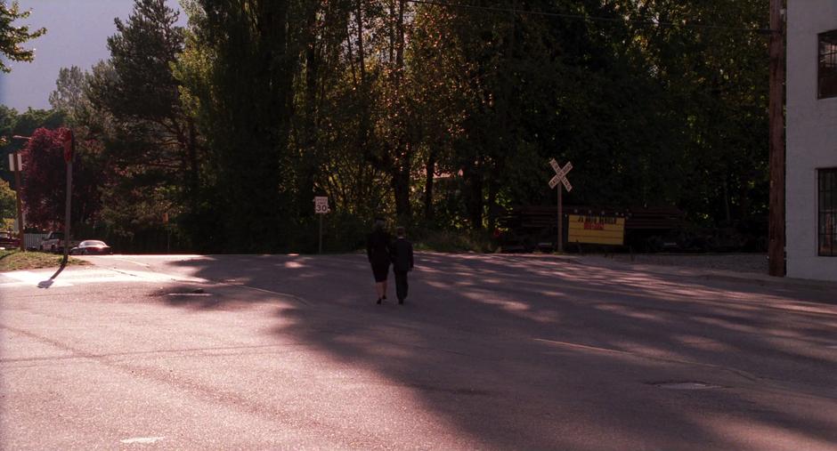 The old woman and masked boy walk away across the street.