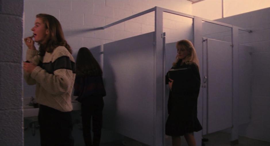 Laura enters a bathroom stall while several other girls stand around the sinks.