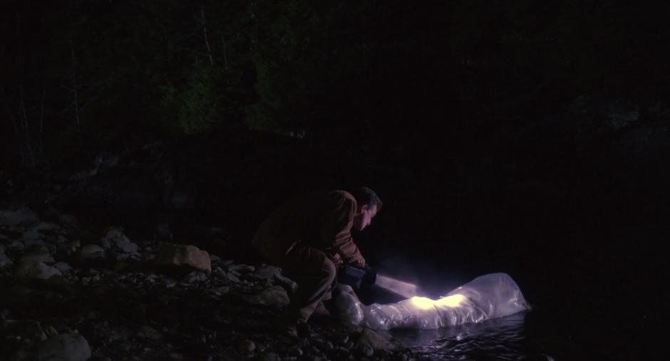 Leland pushes Laura's plastic wrapped body into the water.