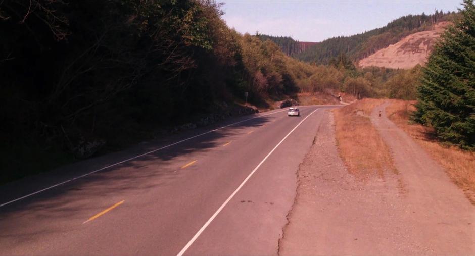 The car drives away from the camera along the highway.