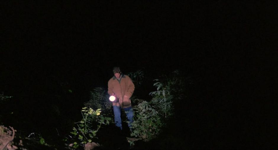 Bobby's drug dealer approaches them through the darkened woods with his flashlight.