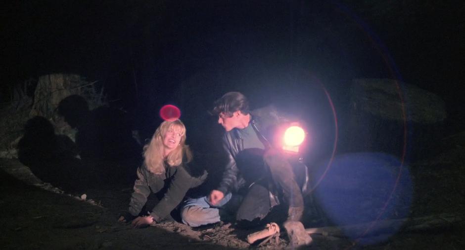 Laura lays on the ground next to Bobby while he points his flashlight at his drug supplier.