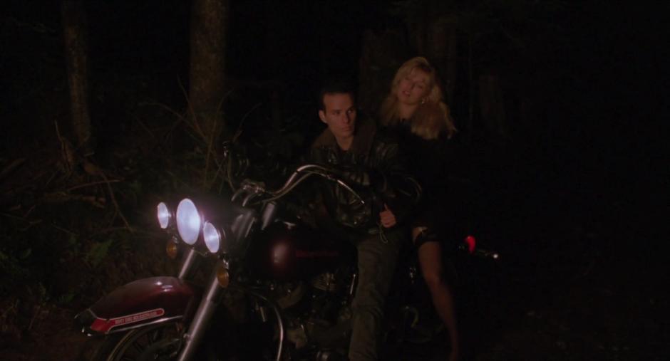 Laura rides into the clearing on the back of James's motorcycle.