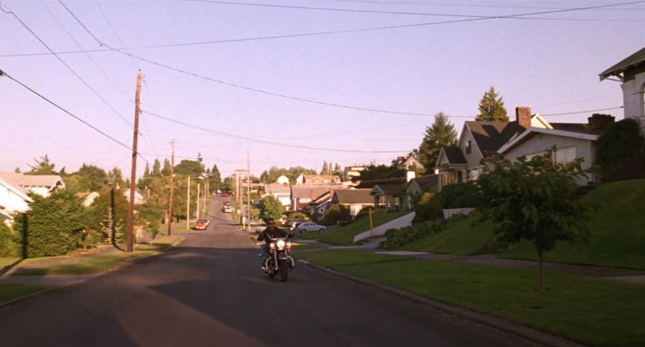 James rides his motorcycle down the street to the Palmer house.