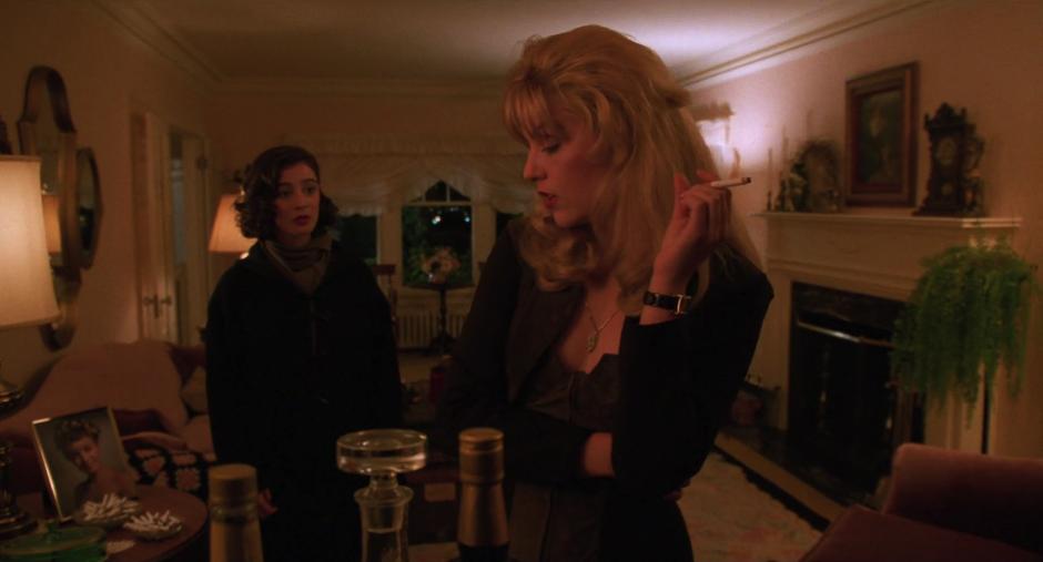 Donna looks at Laura as she stands at the bar with a cigarette.