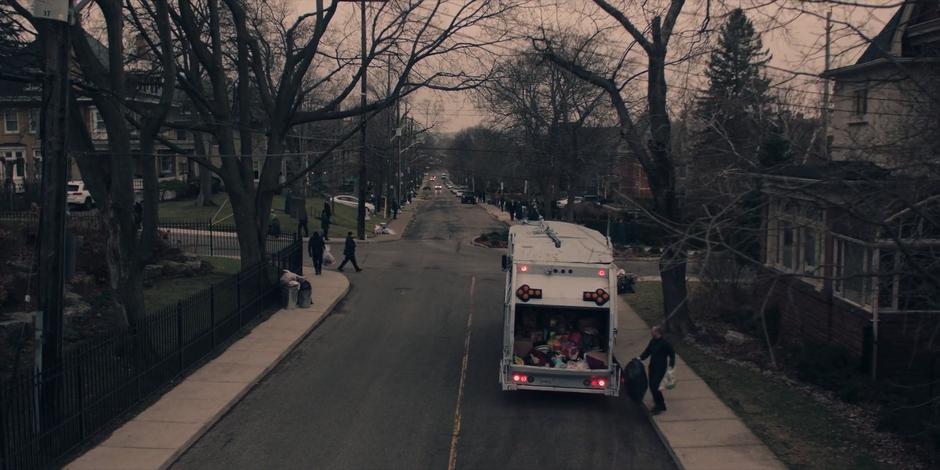 A man collects old clothing to throw into the back of the garbage truck.