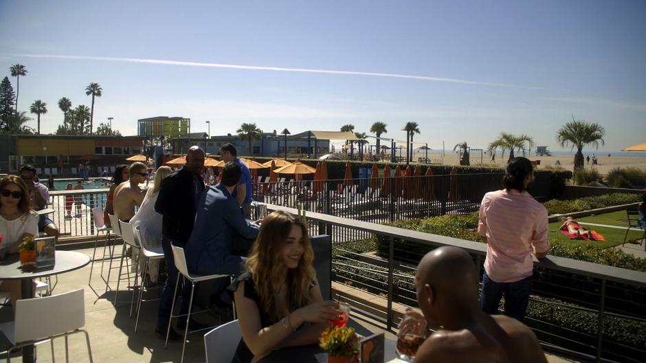 Amenadiel approaches Lucifer where he is sitting at the bar on the beach.