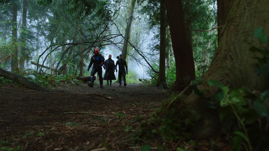 Slade Wilson, Digger Harkness, and Oliver walk down a path in the forest.