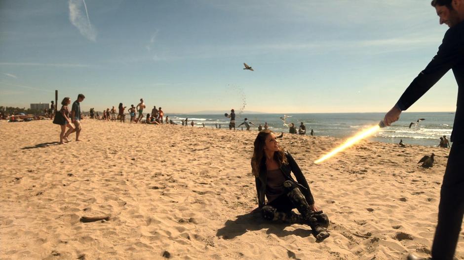 Lucifer holds the flaming sword to Charlotte while she lays on the sand in the middle of the stopped world.