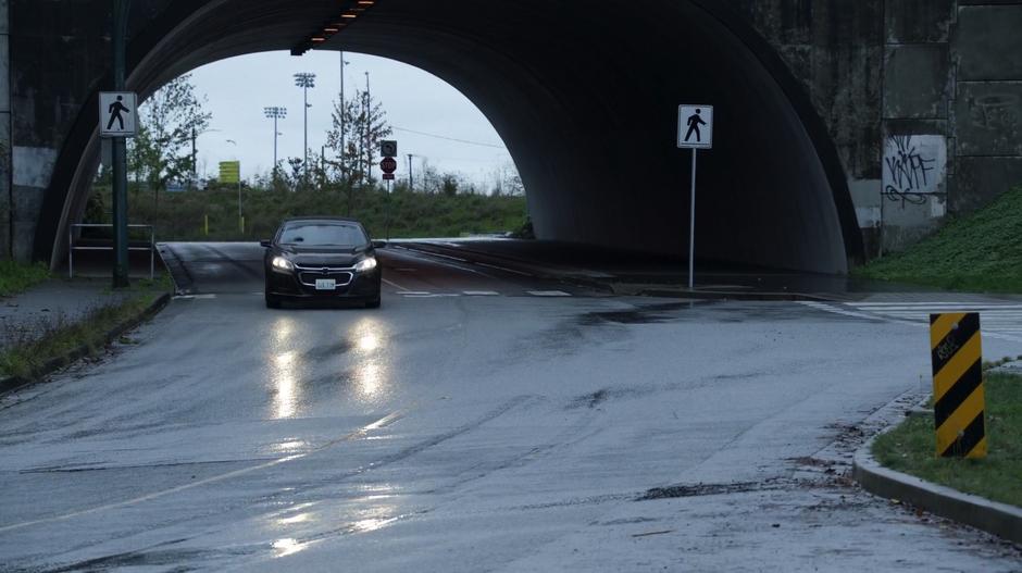 A car drives underneath an underpass at the edge of town.