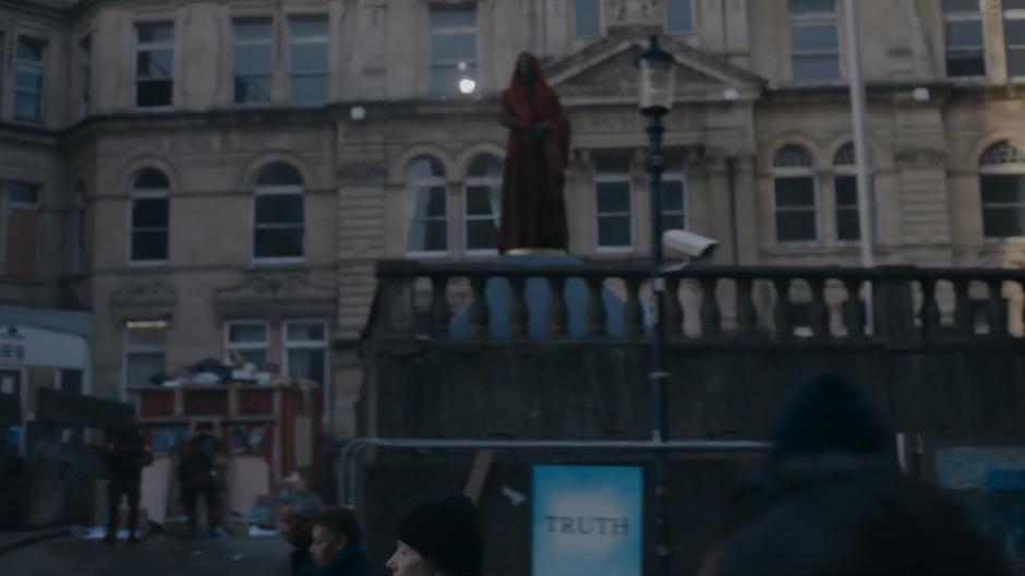 A monk stands elevated above the street while civilians walk past.