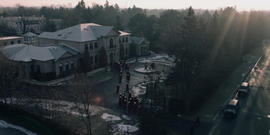 The handmaids assemble out front of the Putnam house to await Janine's departure.