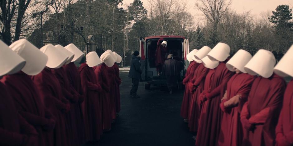 Janine waves down the line of handmaids at Offred from the back of the van.