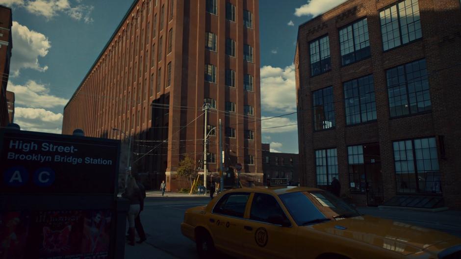 Daytime establishing shot of Magnus's building with the High Street subway station in the foreground.