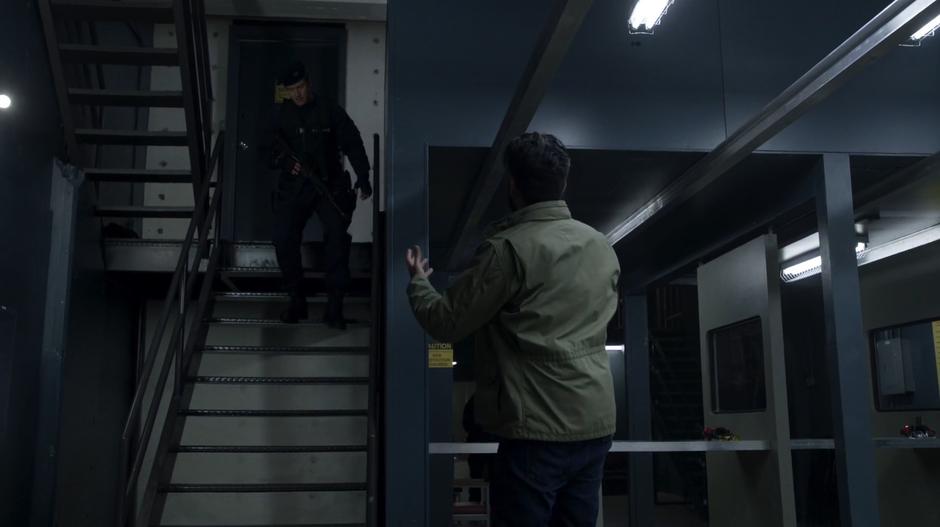 Ravi looks up at Major as he walks down the stairs inside the range.