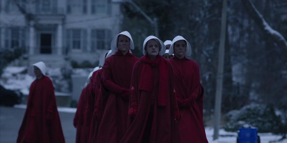 Offred leads the crowd while several handmaids peel off.