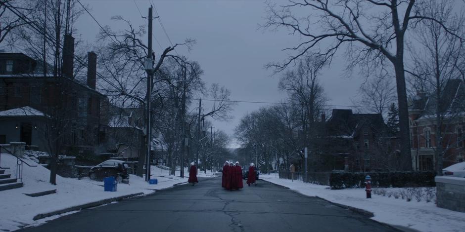 Offred walks in front of a smaller group of handmaids as two more peel off.