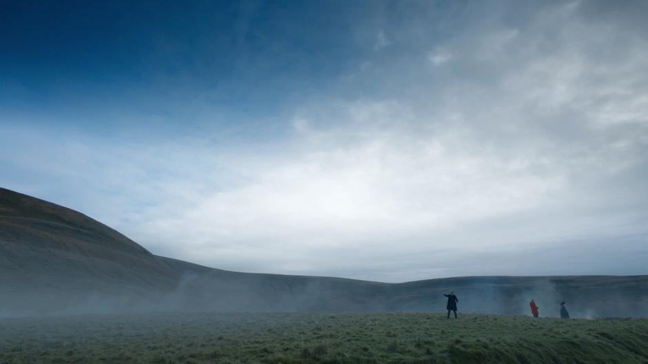 The Doctor points towards the stone cairn while Nardole stands next to a crow.