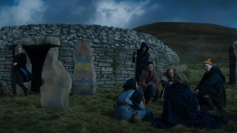 The Doctor exits the cairn while Nardole tells a story to a group of Picts.