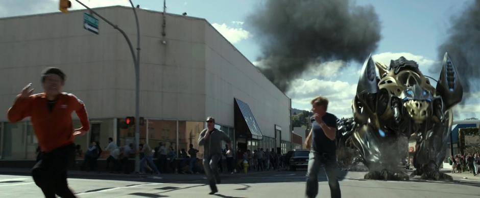 Trini's yellow Zord runs into the intersection while people run from the destruction.