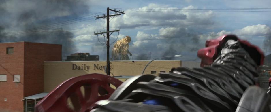 The red Zord looks at Goldar walking past in the distance past the Daily News building.