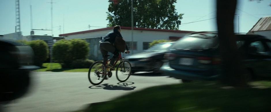 Jason bikes quickly down the street carrying a backpack.