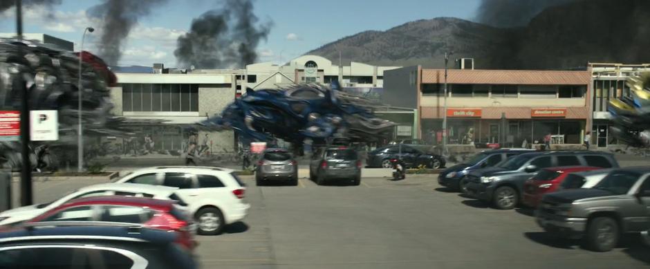 The blue Zord runs down the street across frame and is followed by the black and red Zords.