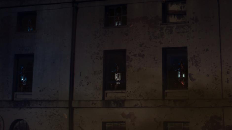 A whole bunch of Cybermen watch from the windows of a building.