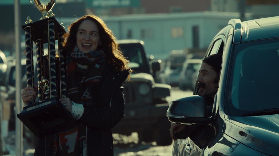 Doc leans his head out of the car door while Wynonna smiles up at the stolen trophy.