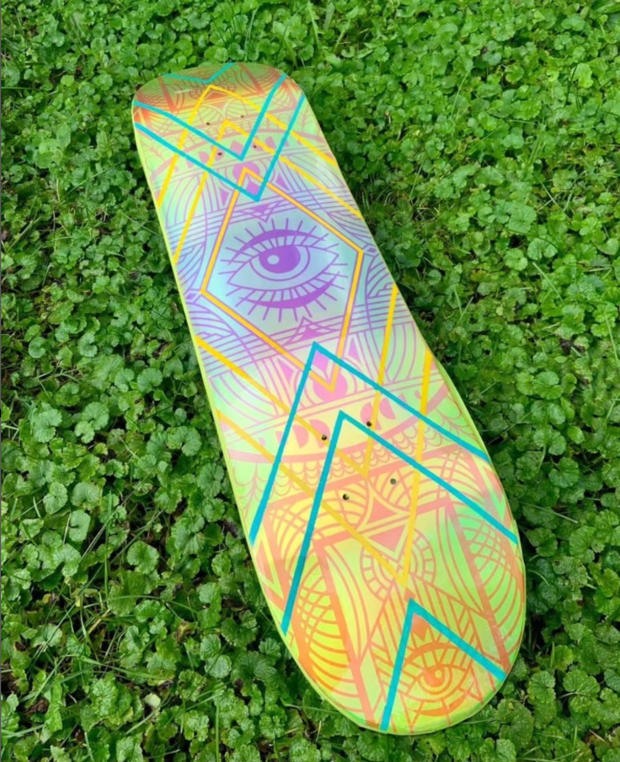 Skateboard painted with eyeball laying on field of clover
