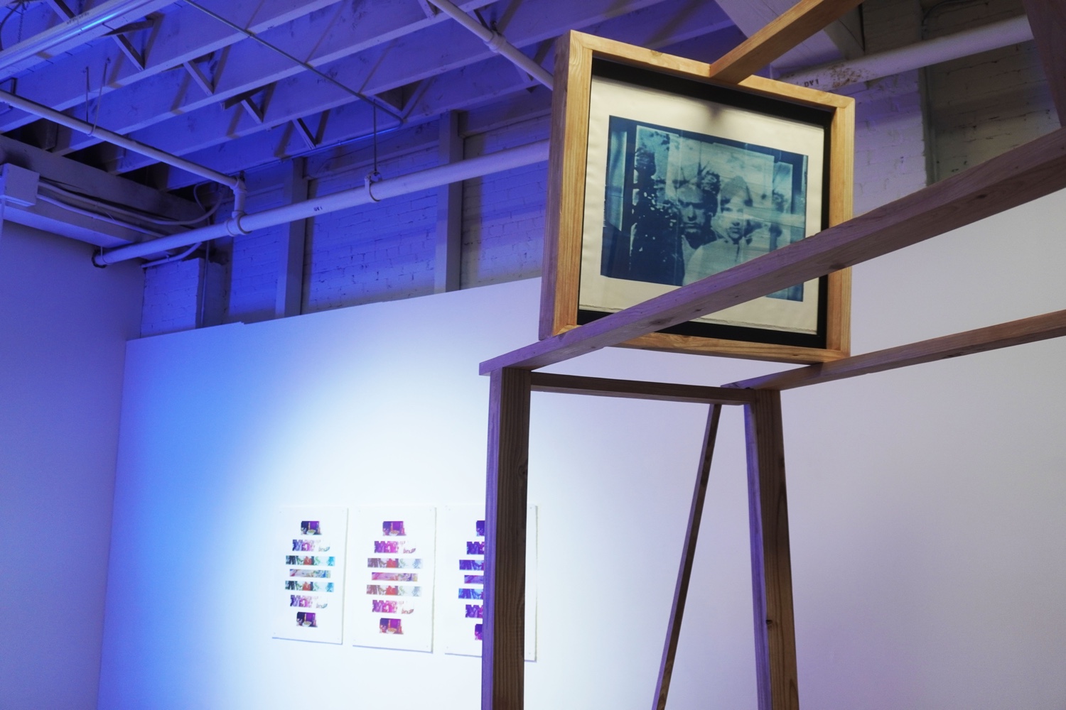 A blue & white photo of a couple framed into a wooden structure in an art gallery