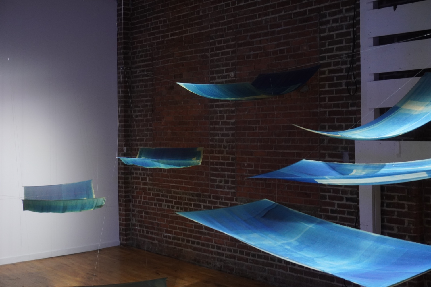 Blue cyanotypes on paper hang horizontally in a room like flying carpets