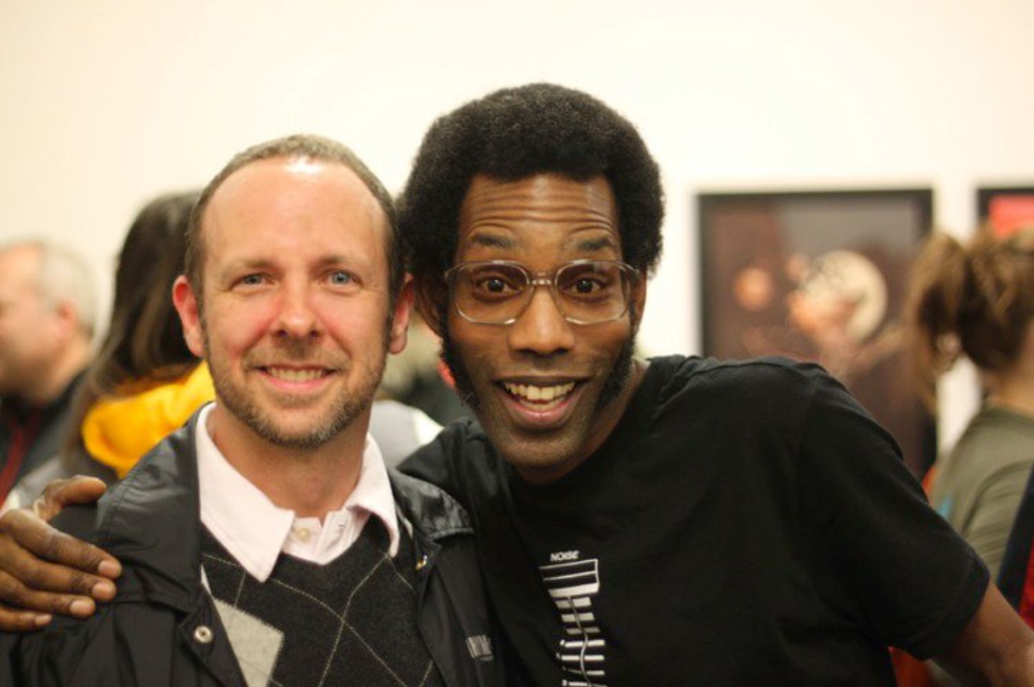 Two men smile and pose at an art opening